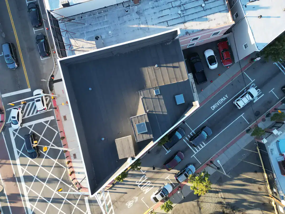 Drone aerial view of a completed torch-down modified bitumen flat roof on a corner mixed-use building in Union City, NJ with new skylights and white parapet coping